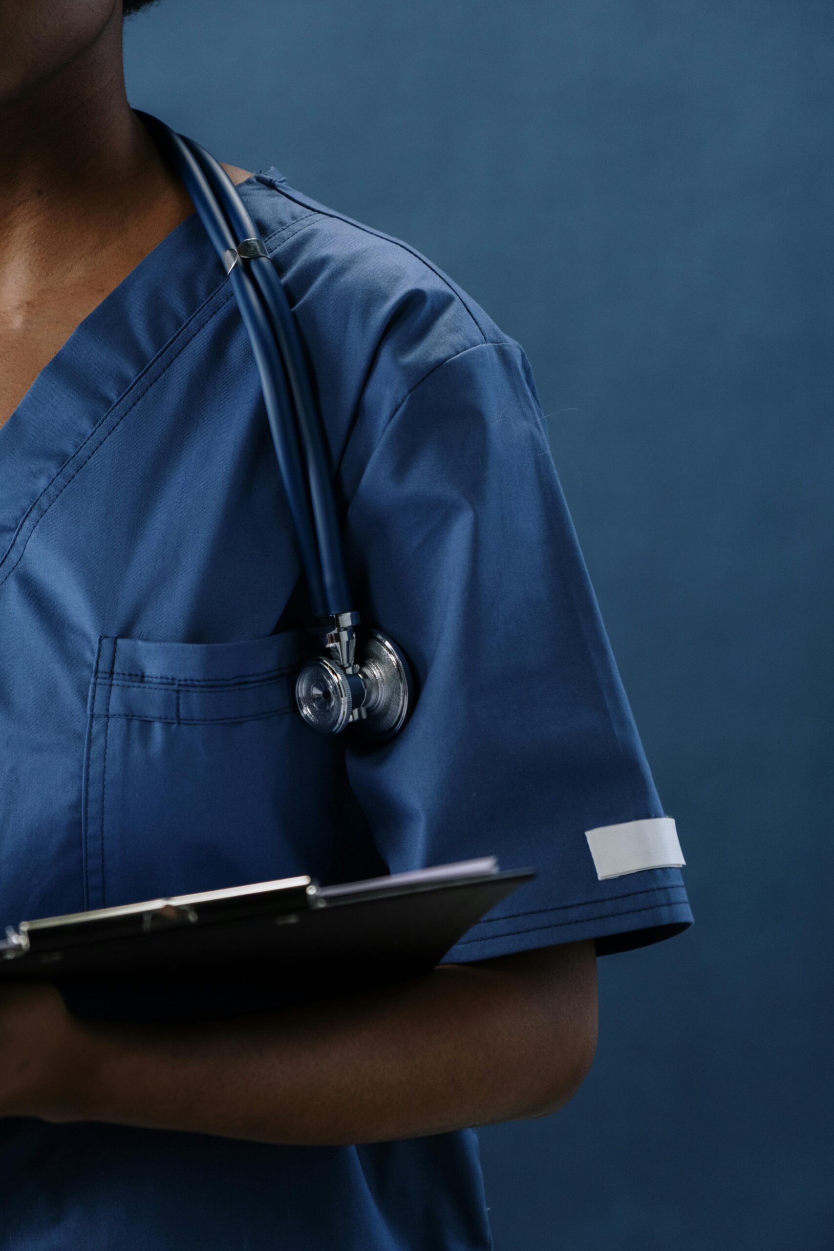 Close-up of a healthcare professional in blue scrubs with a stethoscope and clipboard.